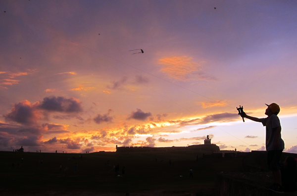 A young boy flys his kite in front of Castillo de San Felipe del Morro as the sun sets in Old San Juan